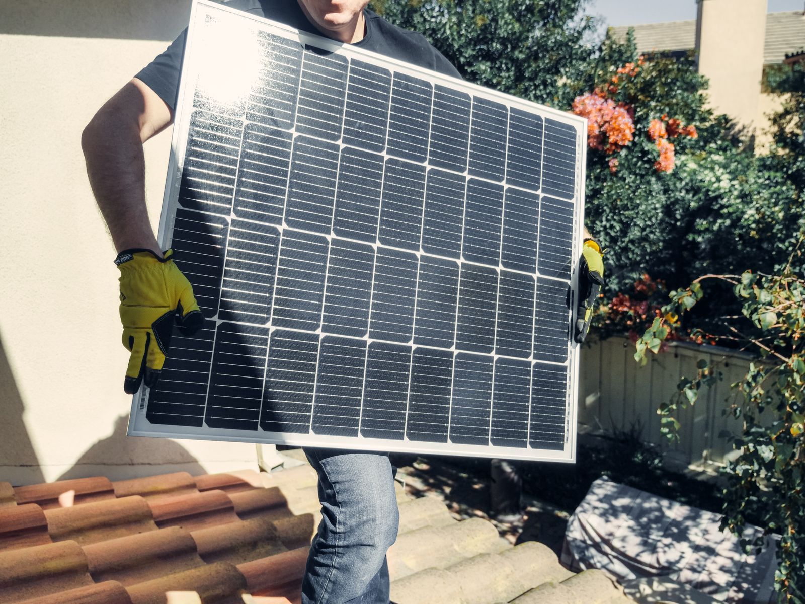 Installateur portant un panneau photovoltaïque sur un toit en tuiles